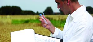 Man holding clipboard in left hand and test tube in right, doing work outside in a field